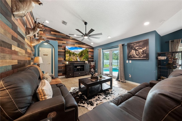 living area with wood walls, vaulted ceiling, a ceiling fan, arched walkways, and light tile patterned floors