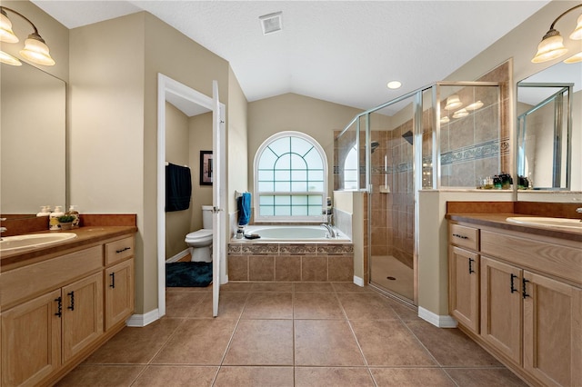 bathroom with a shower stall, vaulted ceiling, tile patterned floors, two vanities, and toilet