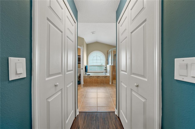 corridor with vaulted ceiling, a textured wall, dark wood finished floors, and a textured ceiling