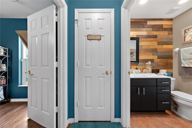 bathroom with toilet, wood walls, vanity, and baseboards