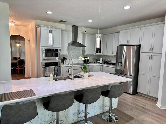 2691 Cypress Tree Trl, Saint Cloud, FL 34772 - kitchen featuring appliances with stainless steel finishes, wall chimney range hood, arched walkways, a breakfast bar area, and light countertops