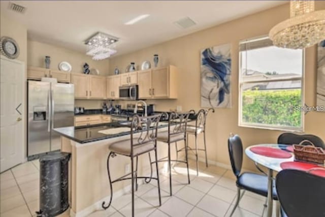 214 Tupelo Cir, Davenport, FL 33897 - kitchen with stainless steel appliances, light brown cabinetry, a peninsula, light tile patterned floors, and a kitchen bar