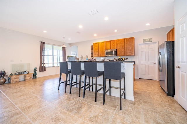 389 Yellow Snapdragon Dr, Davenport, FL 33837 - kitchen with stainless steel appliances, brown cabinets, light tile patterned floors, recessed lighting, and a kitchen bar