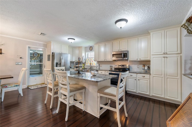 kitchen featuring stainless steel appliances, dark wood-type flooring, a breakfast bar, a kitchen island, and dark stone countertops