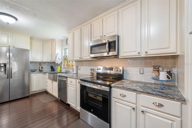 kitchen with stainless steel appliances, a sink, a textured ceiling, backsplash, and dark stone countertops