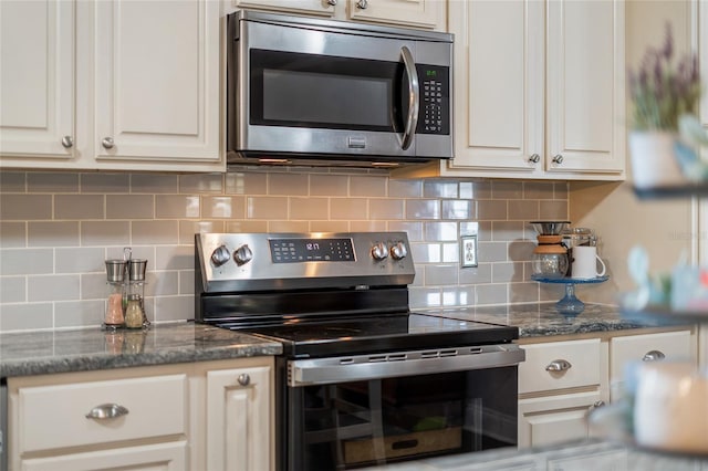 kitchen featuring appliances with stainless steel finishes, decorative backsplash, dark stone countertops, and white cabinetry