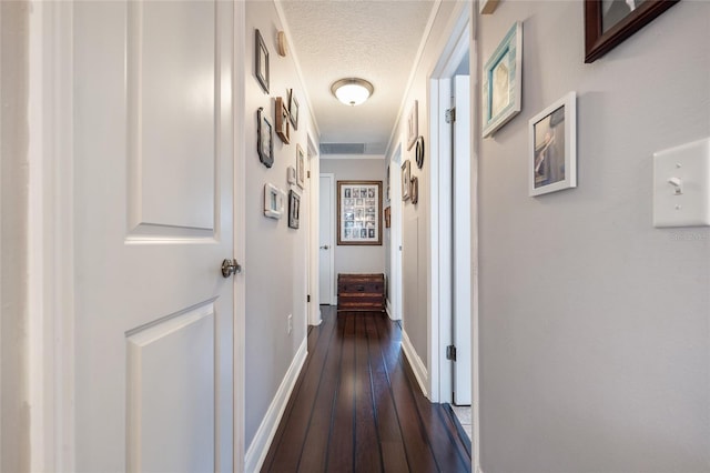hall with dark wood finished floors, a textured ceiling, baseboards, and ornamental molding