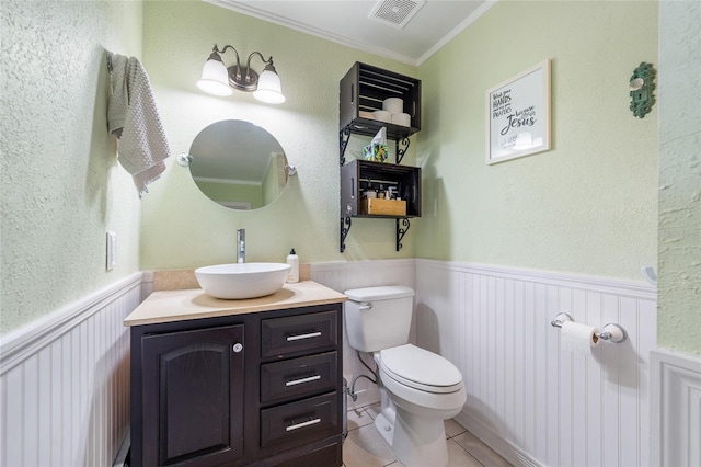 half bath with toilet, ornamental molding, wainscoting, tile patterned floors, and vanity
