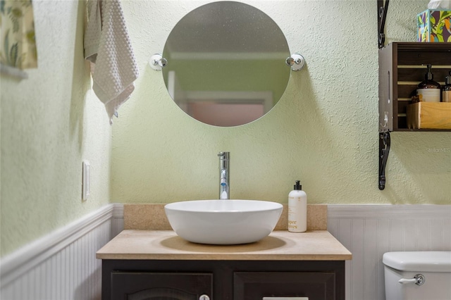 half bathroom featuring wainscoting, toilet, vanity, and a decorative wall