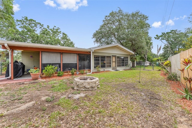 rear view of property with a fire pit, a fenced backyard, and a sunroom