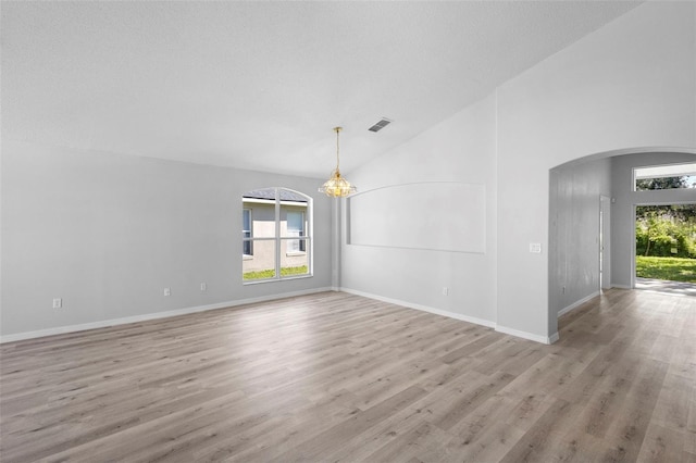 empty room with arched walkways, light wood finished floors, a chandelier, baseboards, and high vaulted ceiling
