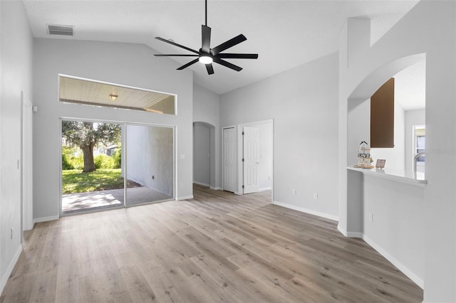 unfurnished living room with arched walkways, ceiling fan, high vaulted ceiling, light wood-style floors, and baseboards