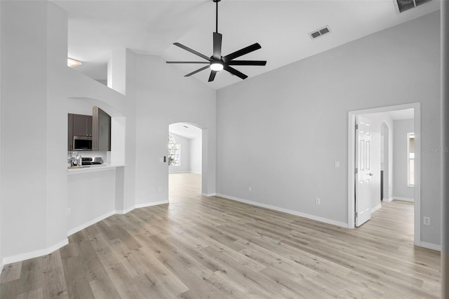 unfurnished living room featuring arched walkways, high vaulted ceiling, a ceiling fan, light wood-type flooring, and baseboards