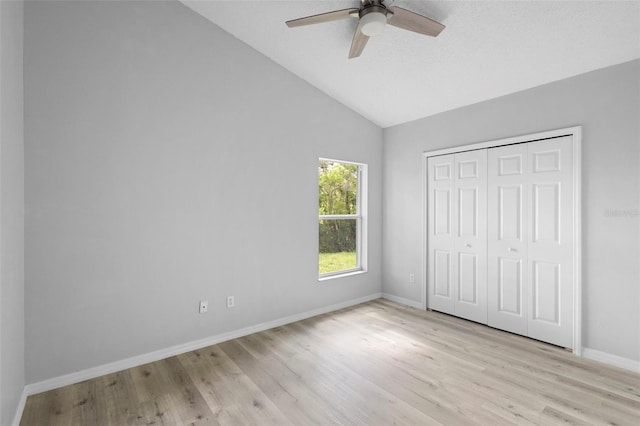 unfurnished bedroom featuring light wood-style floors, lofted ceiling, baseboards, a ceiling fan, and a closet