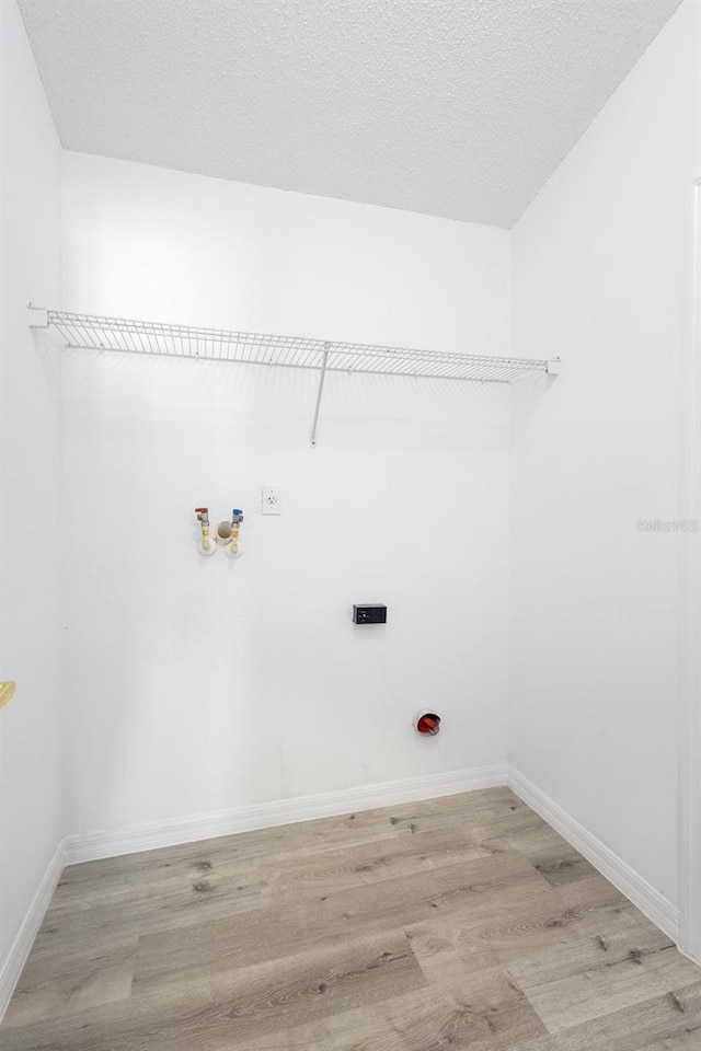 laundry area featuring light wood finished floors, hookup for an electric dryer, baseboards, washer hookup, and a textured ceiling