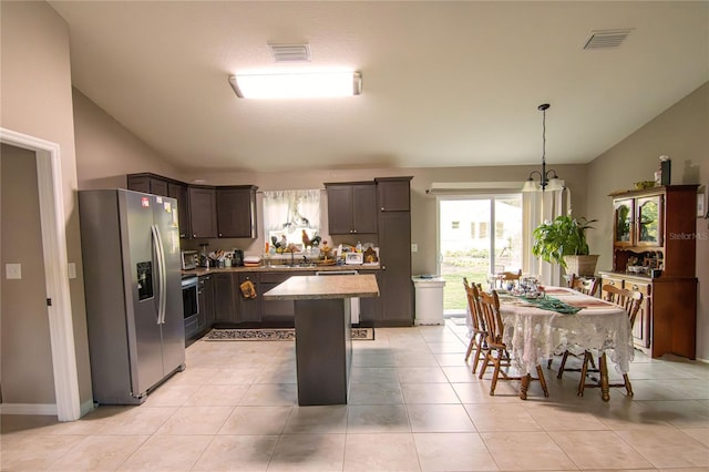 kitchen with stainless steel appliances, lofted ceiling, a sink, light tile patterned flooring, and a center island