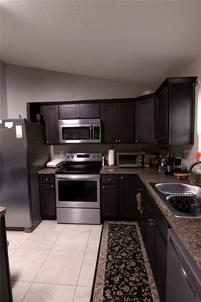 kitchen with appliances with stainless steel finishes, a sink, lofted ceiling, dark countertops, and light tile patterned flooring