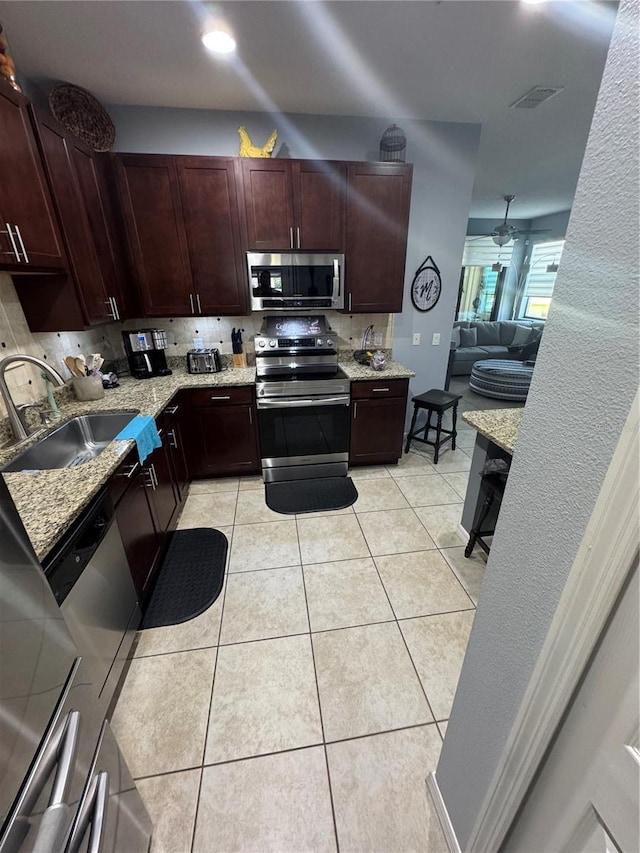 2289 Seven Oaks Dr, Saint Cloud, FL 34772 - kitchen with appliances with stainless steel finishes, a sink, light tile patterned floors, light stone counters, and decorative backsplash