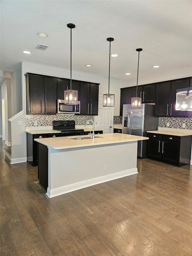 kitchen featuring appliances with stainless steel finishes, a sink, backsplash, dark wood finished floors, and an island with sink