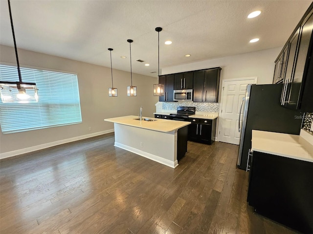 kitchen with appliances with stainless steel finishes, a sink, dark wood-type flooring, a center island with sink, and light countertops