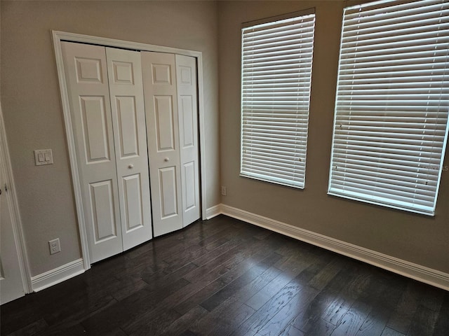 unfurnished bedroom featuring baseboards, a closet, and dark wood finished floors