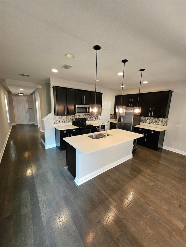 kitchen with stainless steel appliances, a sink, dark cabinetry, backsplash, and recessed lighting