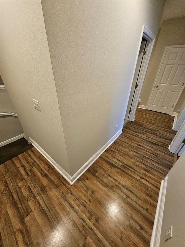 hall featuring dark wood-type flooring and baseboards