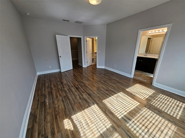 unfurnished bedroom featuring wood finished floors, a walk in closet, baseboards, and ensuite bath