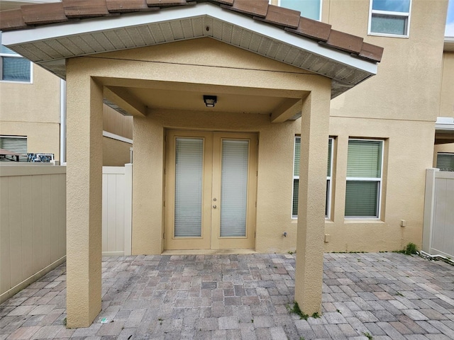 view of exterior entry featuring french doors, stucco siding, and fence