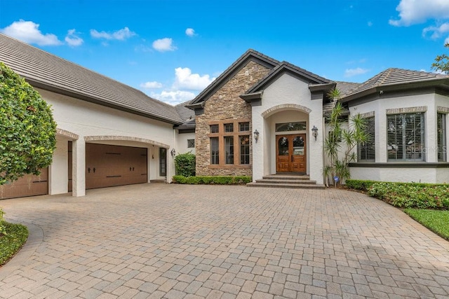 french country style house with french doors, stucco siding, stone siding, and curved driveway