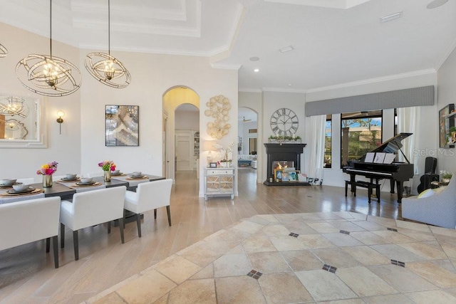 living room with arched walkways, ornamental molding, a chandelier, light wood finished floors, and a tray ceiling