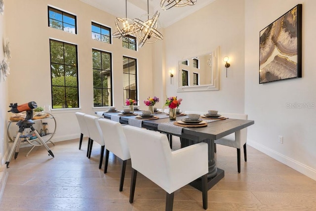 dining room featuring a chandelier, baseboards, light wood finished floors, crown molding, and a high ceiling