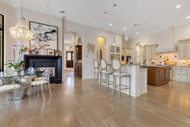 kitchen with custom exhaust hood, arched walkways, a kitchen breakfast bar, cream cabinets, and recessed lighting