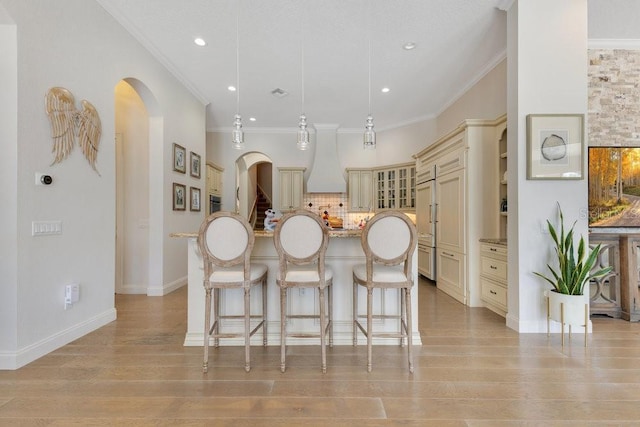 kitchen featuring cream cabinets, custom exhaust hood, arched walkways, a breakfast bar area, and a kitchen island with sink
