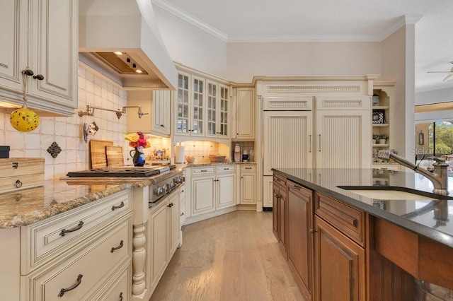 kitchen with cream cabinets, custom exhaust hood, a sink, dark stone counters, and ornamental molding