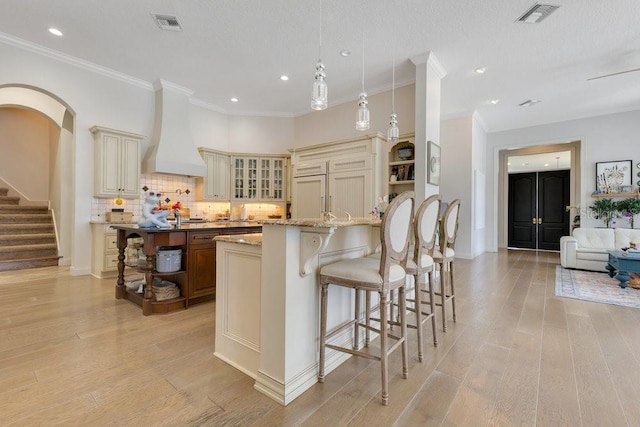 kitchen with cream cabinets, custom range hood, a kitchen bar, open shelves, and recessed lighting