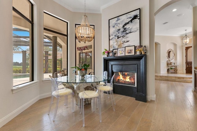 dining space featuring arched walkways, hardwood / wood-style flooring, ornamental molding, a glass covered fireplace, and a chandelier