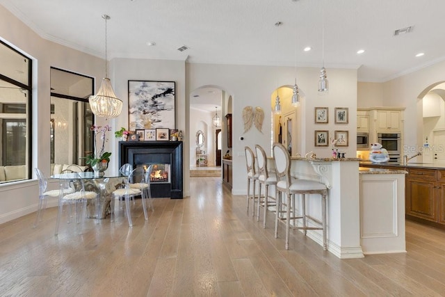 kitchen featuring appliances with stainless steel finishes, arched walkways, a kitchen breakfast bar, light stone countertops, and light wood-type flooring