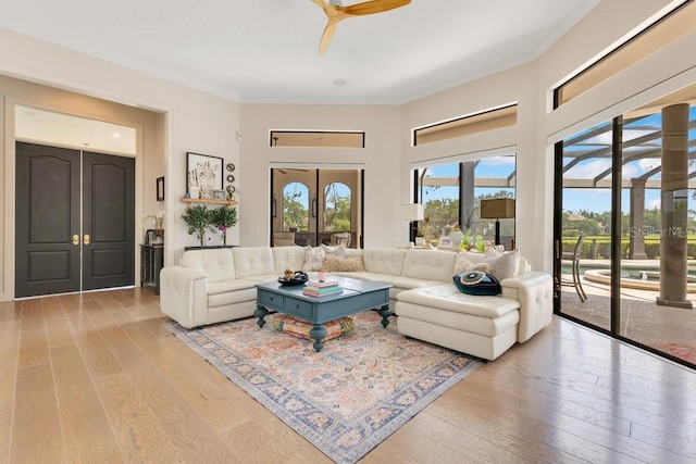 living area featuring ornamental molding, light wood-style flooring, a ceiling fan, and french doors
