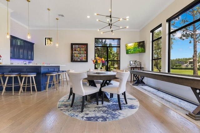 dining room featuring plenty of natural light, light wood-style flooring, crown molding, a chandelier, and bar area