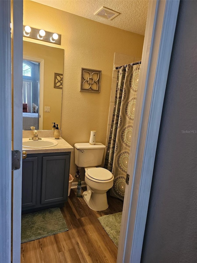 bathroom with a textured wall, wood finished floors, toilet, vanity, and curtained shower