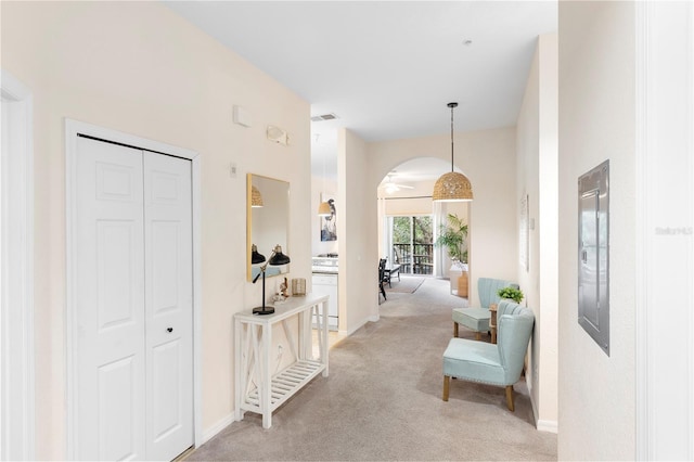 hall featuring arched walkways, light colored carpet, and baseboards
