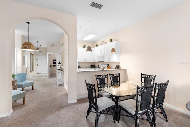 dining area featuring arched walkways, light colored carpet, and baseboards