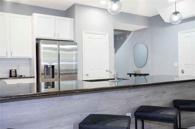 3181 Tocoa Cir, Kissimmee, FL 34746 - kitchen featuring stainless steel fridge with ice dispenser, dark stone countertops, a sink, white cabinetry, and a breakfast bar