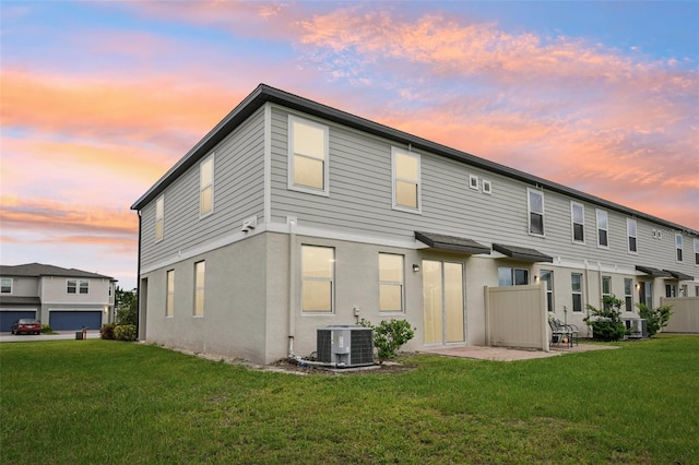 back of property at dusk with a yard, central AC unit, and stucco siding