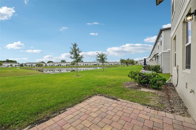 view of green lawn with a water view and a patio area