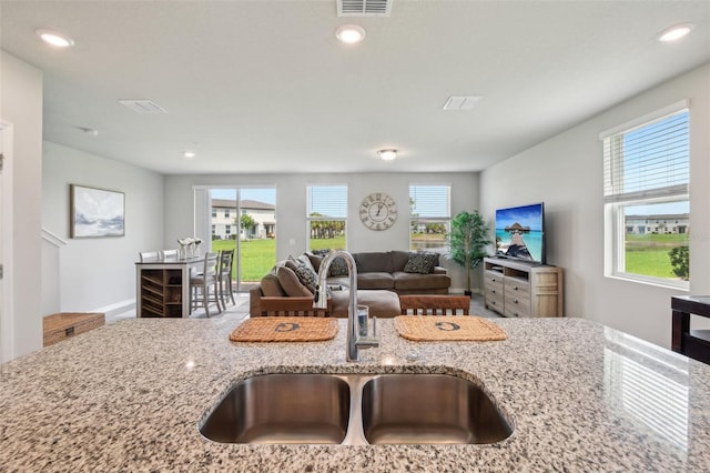 kitchen with a sink, plenty of natural light, light stone counters, open floor plan, and recessed lighting