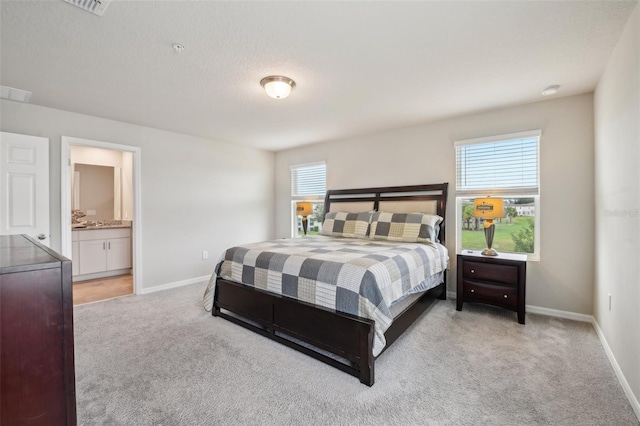 bedroom with light carpet, baseboards, and ensuite bath