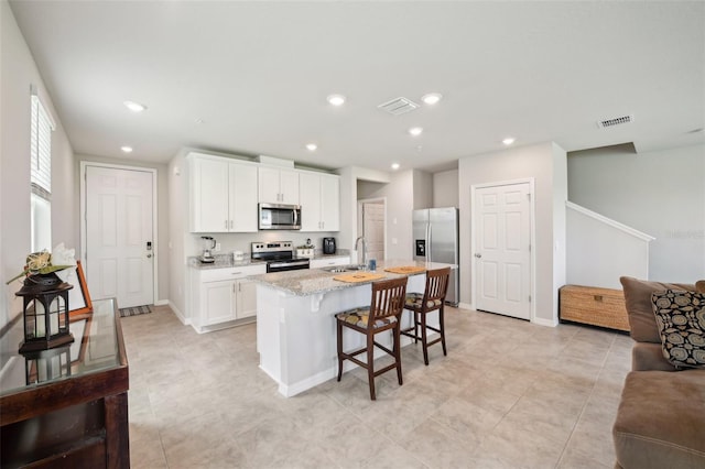 kitchen featuring stainless steel appliances, light stone countertops, open floor plan, a kitchen bar, and white cabinetry