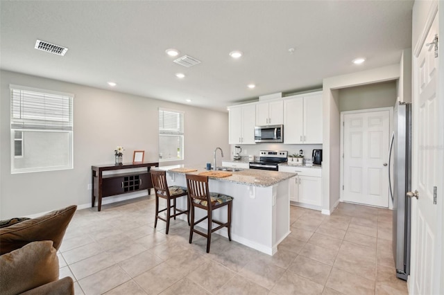 kitchen with appliances with stainless steel finishes, a sink, a center island with sink, white cabinets, and a breakfast bar area